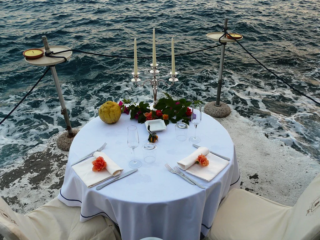 A candlelit table for two set on a whitewashed terrace above the sea
